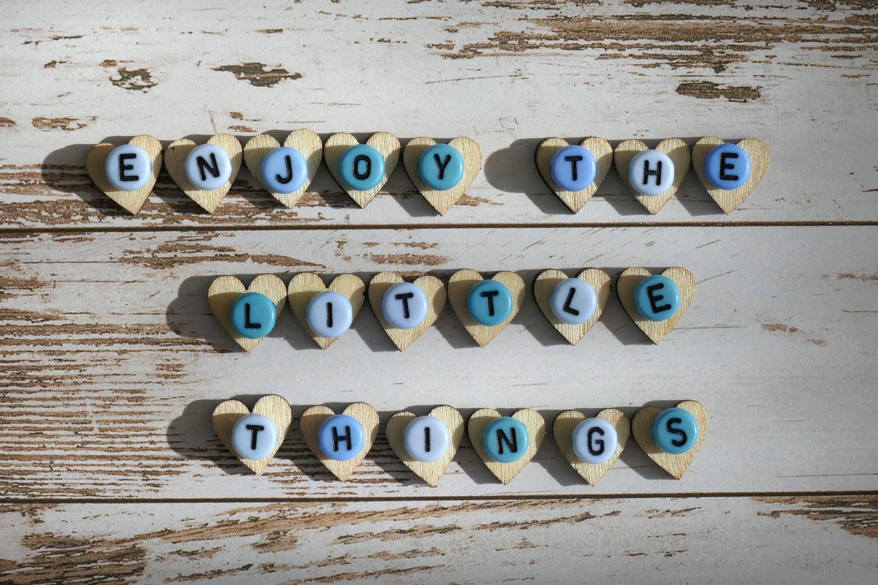 Heart-shaped letters spelling 'Enjoy the Little Things' on a rustic wooden background for inspirational decor.