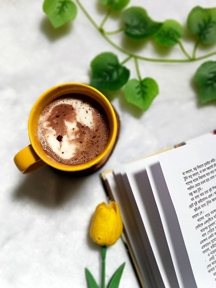 A warm and cozy setting with coffee, a book, and a yellow tulip, perfect for relaxation.
