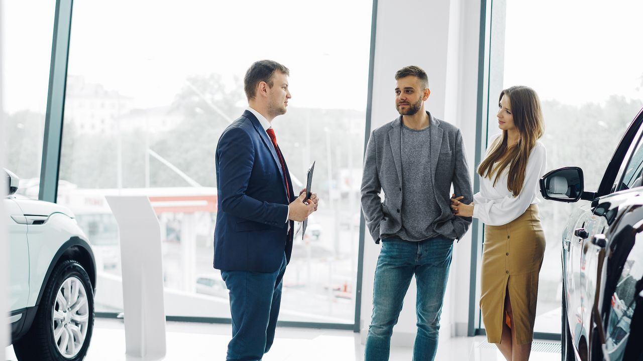 services-img Business professional consulting a couple in a modern car dealership setting.